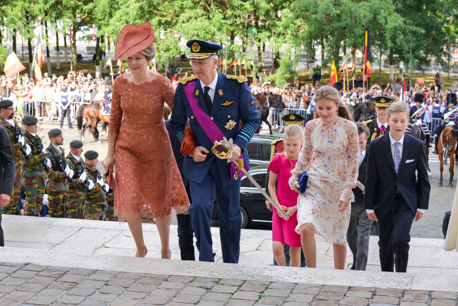 La Reine Mathilde monte les escaliers avec sa famille et porte le chapeau Birdy couleur cuivre.